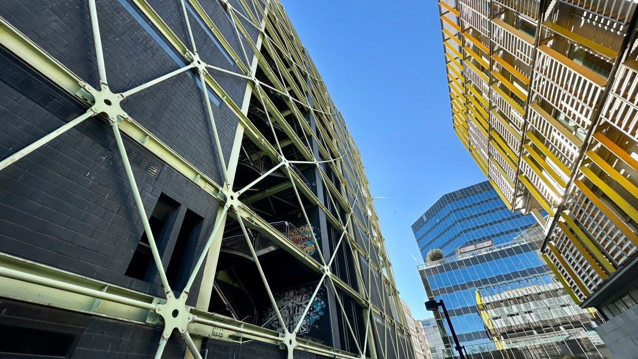 Looking up at the Edificio MediaTIC office building, which is made of glass panels and designed in a geometric angular shape. Other tall, modern office buildings are captured in the image of the Poblenou neighborhood in Barcelona, Spain. 

