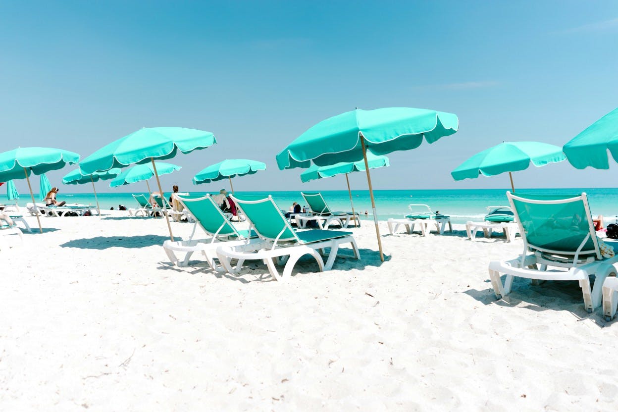 White sand Key Biscayne beach with aqua blue umbrellas and lounge chairs facing clear, blue waters. 