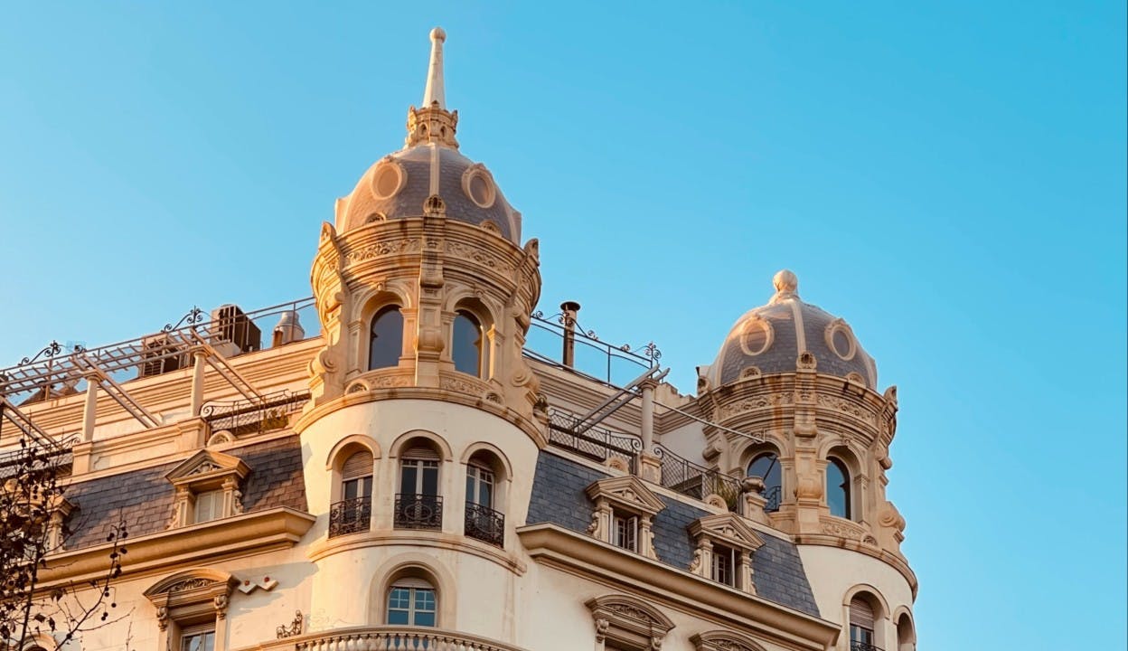 An ornately designed and constructed building in the Eixample neighborhood of Barcelona. With crown details and balconies, the building glows at sunset with trees peaking out from below. 