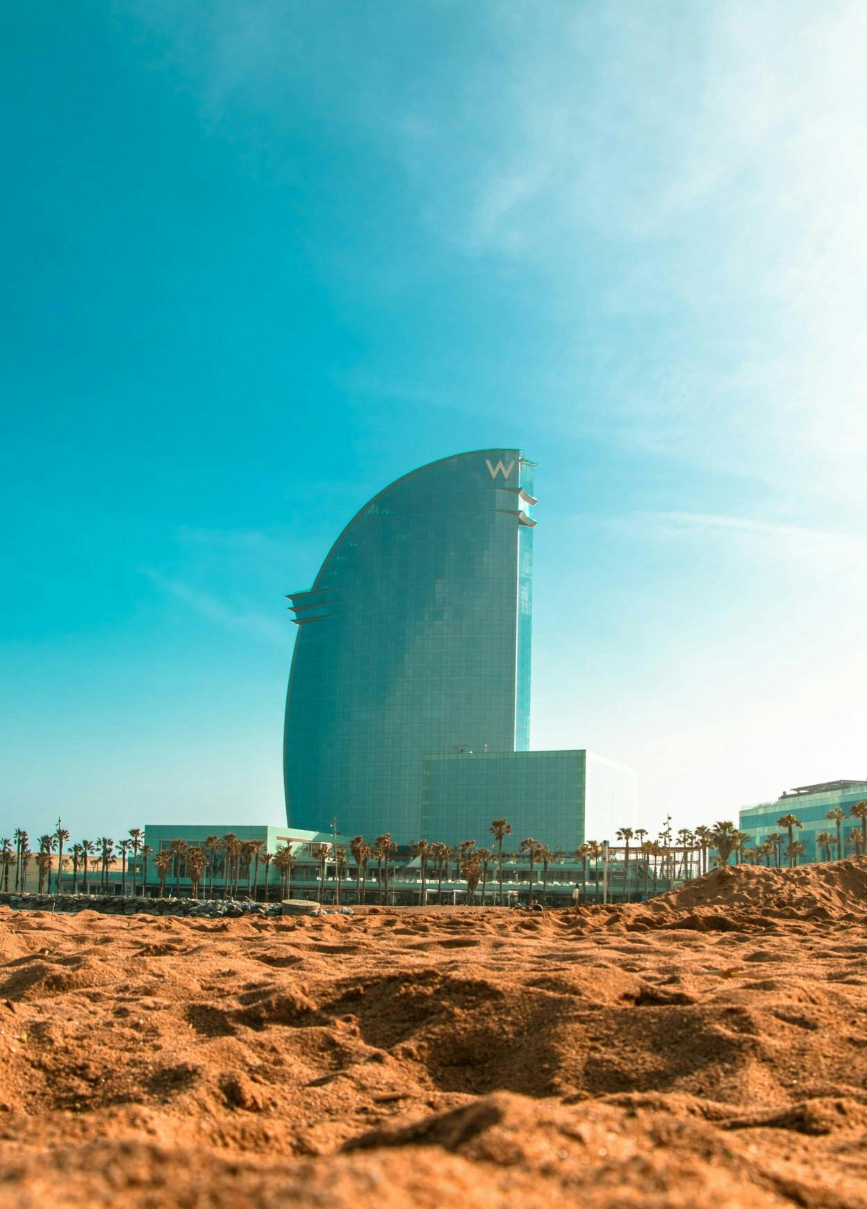 The W Hotel Barcelona, shaped like a wing, protrudes from the landscape and the sandy beach in the foreground. 